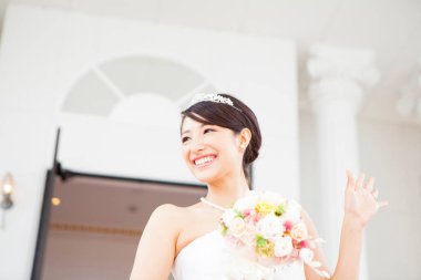 Beyaz elbiseli Asyalı genç gelin elinde buket tutuyor.