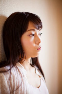 Genç Asyalı kadın dikkatlice yukarı bakıyor, duvara yaslanıyor.