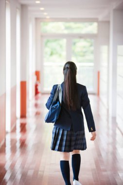 Okul salonunda çantalı, üniformalı genç bir kızın arka görüntüsü.