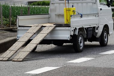 Caddede tahta rampaları olan küçük beyaz bir kamyon park etmiş.