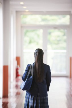 Okul salonunda çantalı, üniformalı genç bir kızın arka görüntüsü.
