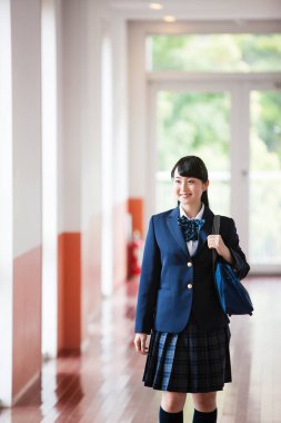 Okul salonunda, üniformalı, çantalı Asyalı bir kızın portresi.