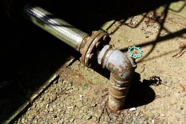 Paslı boru tesisatı ve valf, çakıl yolunun yakınındaki bir inşaat alanında.