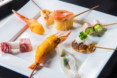 Şiş deniz ürünleri ve suşinin lezzetli çeşitleri lüks bir lokantada beyaz bir tabakta servis ediliyor.