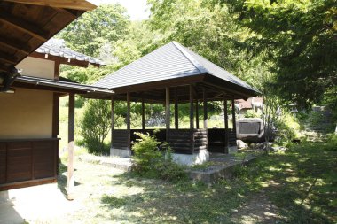 Yeşil ağaçlar ve çimlerle çevrili geleneksel ahşap çardak.