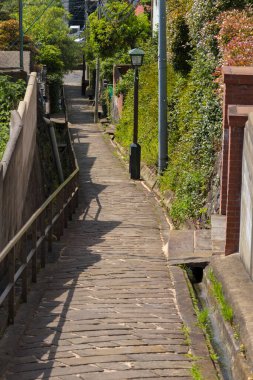 Yeşil çitler ve tuğla duvarlar arasında dolanan dar taş patika.