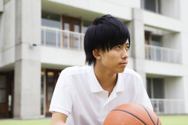 Sahada elinde basketbol topu tutan genç bir Japon.