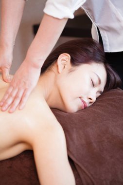 Genç Asyalı kadın güzellik salonunda sırt masajı yaptırıyor.