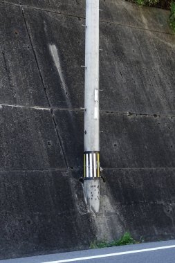 Eğimli istinat duvarına karşı duran uzun beton elektrik direği