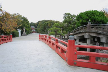 Etrafı yeşilliklerle çevrili kırmızı köprü taş patikadan geçiyor.