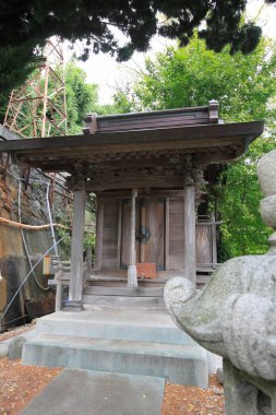 Yeşil ağaçlar ve taş heykellerle çevrili küçük ahşap bir tapınak.