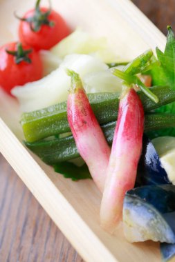 Fresh vegetables including radishes tomatoes okra arranged on wooden tray