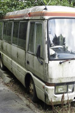 Çatlamış otların yanına park edilmiş terk edilmiş paslı minibüs.