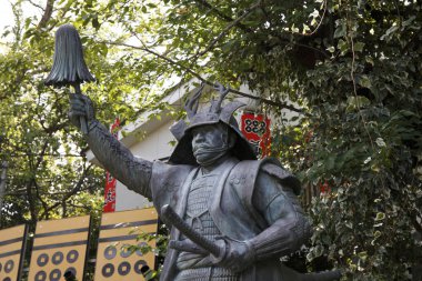 Japon parkının bereketli yaz yeşilliği arasında eskimiş bir figürü yakalıyorum..