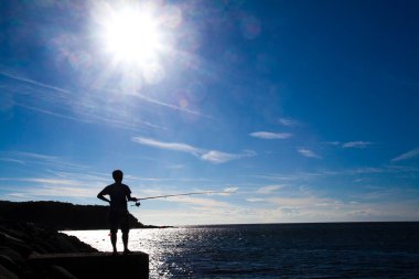 Güneş doğarken elinde olta olan balıkçının silueti. 