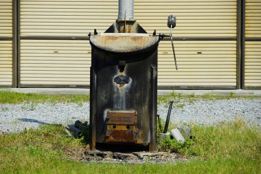 Binanın yanındaki çakılların üzerinde duran paslı metal yapı.