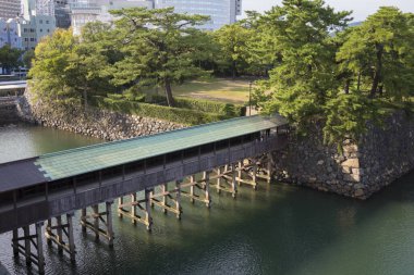 Tahta köprü, taş duvar ve ağaçların yanında durgun suyu geçiyor.
