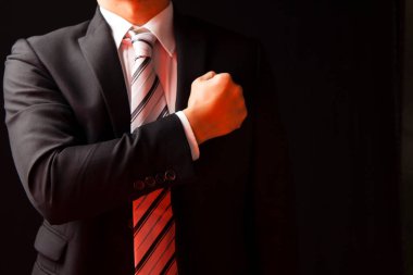 Siyah takım elbiseli iş adamı, siyah arka planda sol göğsüne yumruk atarak güven gösteriyor.