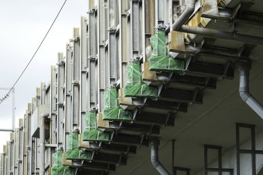 Yeşil balkonların ve metal yapıların tekrarlandığı modern bina cephesi