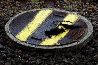 Sarı çizgili çakılların üzerinde duran paslı rögar kapağı.