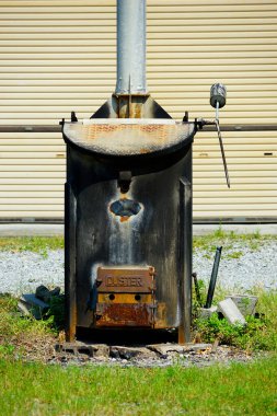 Bej duvarın önünde duran paslı metal soba.