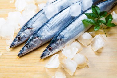 Yeşil yapraklı çiğ uskumru balığı ve ahşap zemin üzerinde buz küpleri