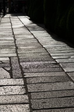 Güneş ışığı, taşlı kaldırım boyunca gölgeler bırakıyor.