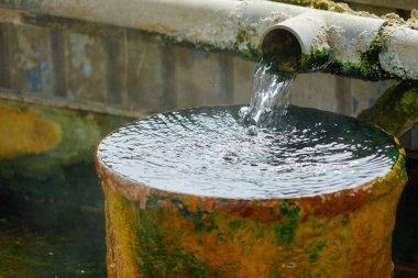 Dışarıdaki paslı yosun kabını dolduran borudan akan temiz su.