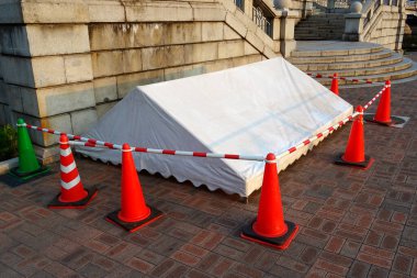 Turuncu trafik konileriyle çevrili beyaz çadır.