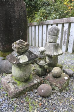 Yıpranmış taş fenerler ve ahşap çitlerin yanında duran yosunlu heykeller.