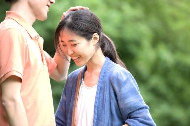 Asyalı bir adam dışarıda kız arkadaşının kafasını okşuyor.