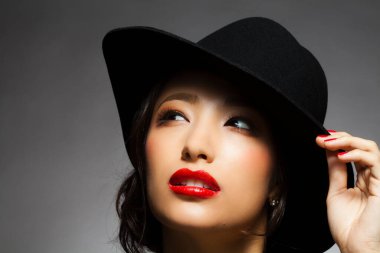 Kırmızı dudaklı ve siyah şapkalı güzel Asyalı kadın portresi.