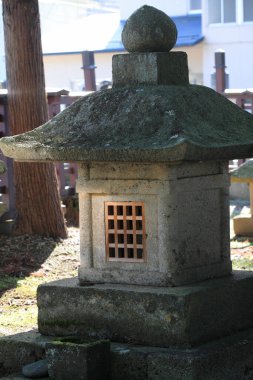 Güneş ışığında ağacın yanında duran yıpranmış taş fener.