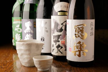 Seramik bardakların arkasında duran çeşitli Japon sake şişeleri.