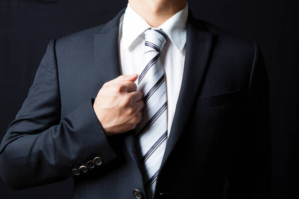 cropped image of businessman wearing suit and tie on dark background