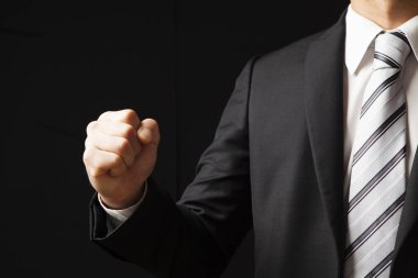 Siyah takım elbiseli ve beyaz gömlekli Asyalı işadamı siyah arka planda yumruğunu gösteriyor.