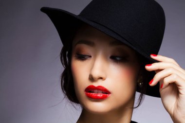 Kırmızı dudaklı ve siyah şapkalı güzel Asyalı kadın portresi.