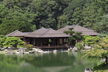 Geleneksel Japon evi, sakin yeşil göletin yanında yansıyor.