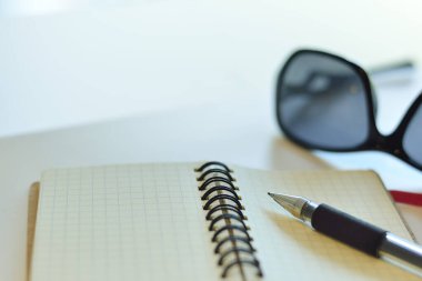 Masadaki defter, güneş gözlüğü ve kalem. 