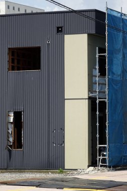 İnşaat halindeki modern bina iskelesi ve mavi güvenlik ağı içeriyor.