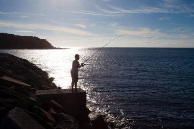 Güneş doğarken elinde olta olan balıkçının silueti. 
