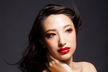 Güzel Asyalı kadın kırmızı dudaklarıyla poz veriyor ve başka tarafa bakıyor.
