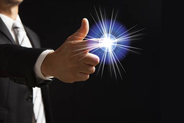 Takım elbiseli bir adamın, sanki elinden ateşleniyormuş gibi dijital olarak eklenmiş bir kristal küreyle parmak tabancası hareketi yaptığını gösteren bir kompozit..