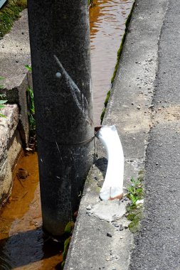 Kahverengi su kanalının yakınındaki beton kaldırımın yanındaki beyaz eğimli boru.