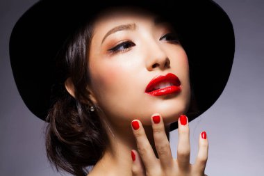 Siyah arka planda parlak makyajlı şapkalı genç bir kadının portresi.