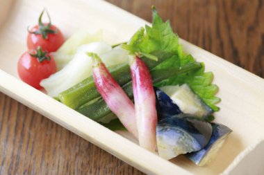 Fresh vegetables and pickled fish arranged on wooden plate