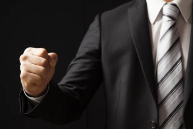 Siyah takım elbiseli ve beyaz gömlekli Asyalı işadamı siyah arka planda yumruğunu gösteriyor.