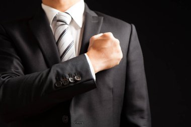 Siyah takım elbiseli iş adamı, siyah arka planda sol göğsüne yumruk atarak güven gösteriyor.