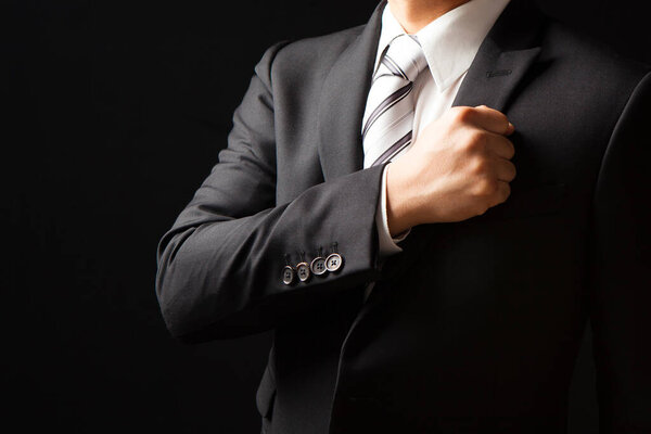 businessman in black suit showing trust by put his fist on left chest on black background