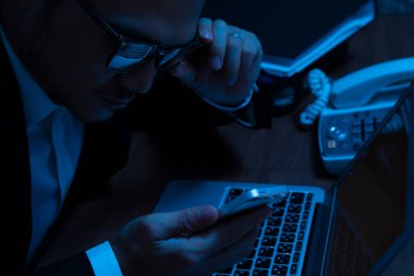 Gözlüklü bilgisayar korsanı karanlık odada akıllı telefon kullanıyor.                          